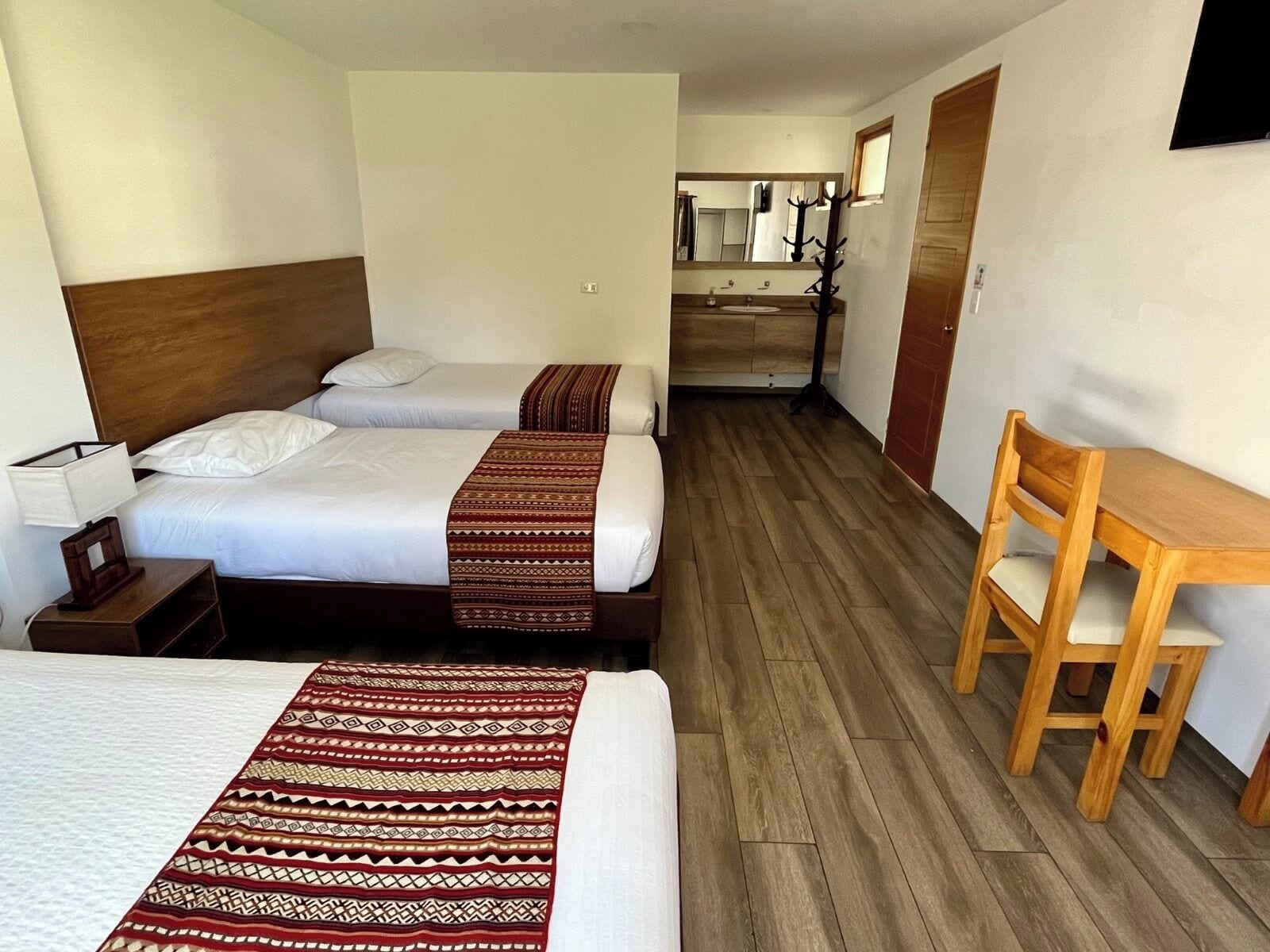 A hotel room with two beds, a wooden desk, a chair, a nightstand, and a mirror.