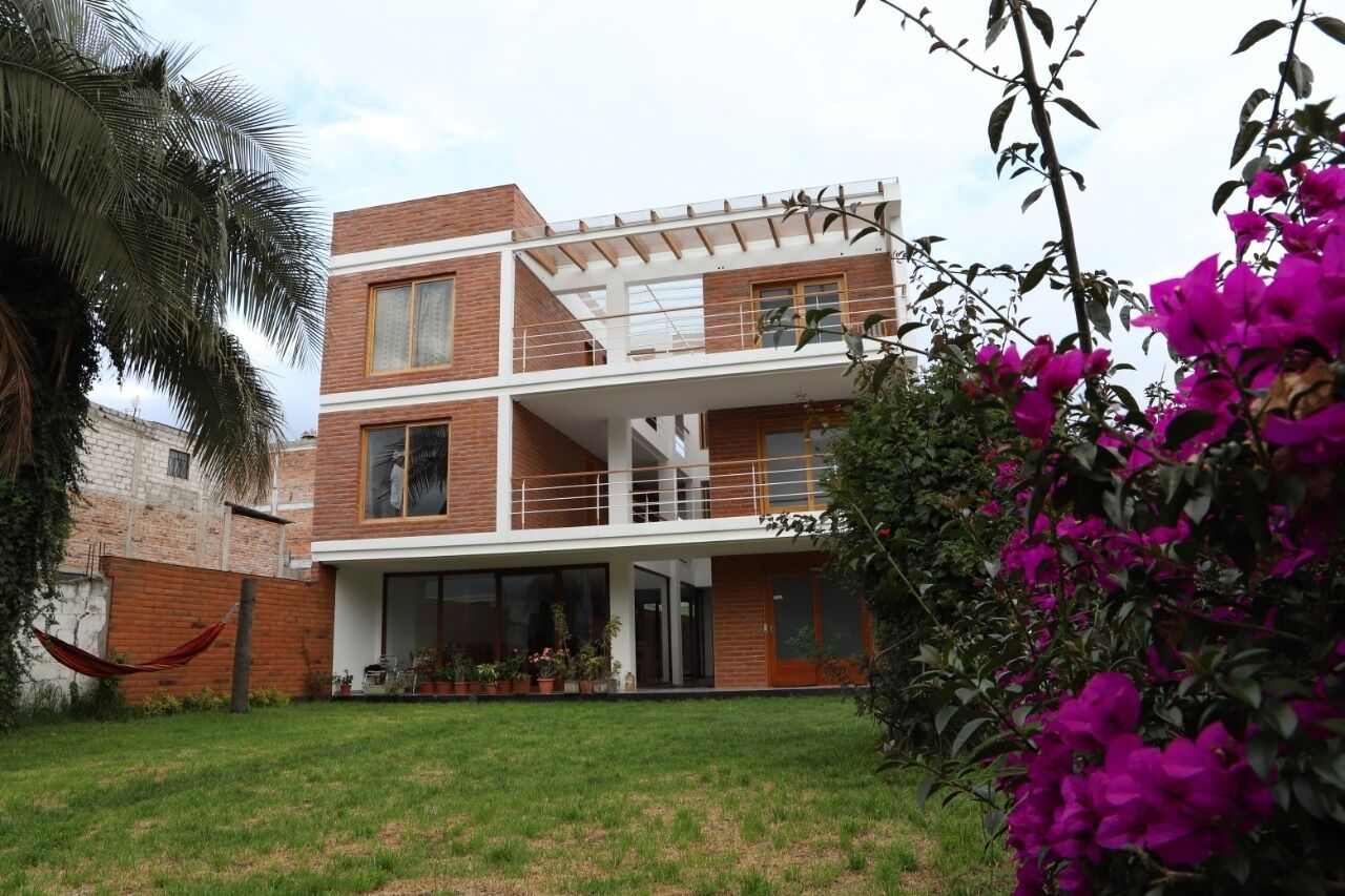 A modern two-story house with a balcony, a grassy yard, and a hammock.
