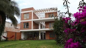 A modern two-story house with a balcony, a grassy yard, and a hammock.