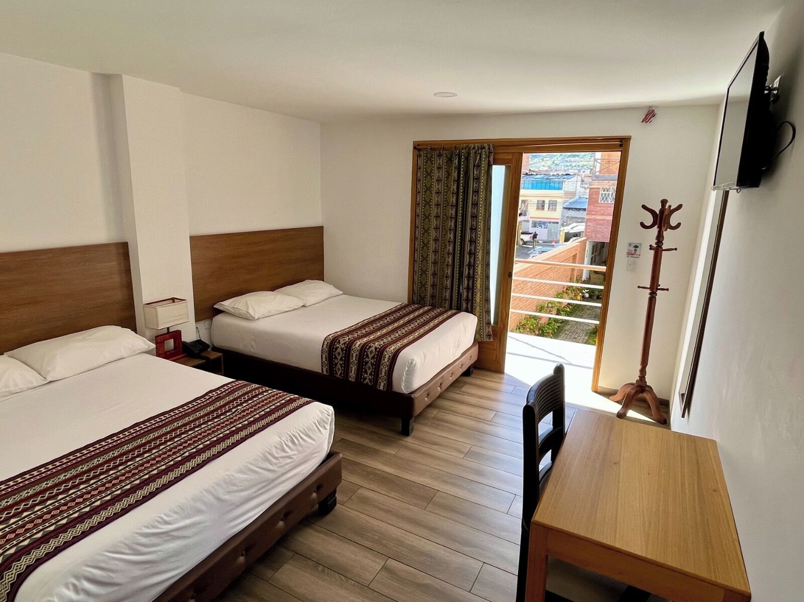 A hotel room with two beds, a wooden desk, a coat rack, and a TV.