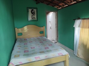 Quarto pequeno com uma cama de solteiro, cabeceira de madeira, parede verde e porta que dá para outro cômodo.