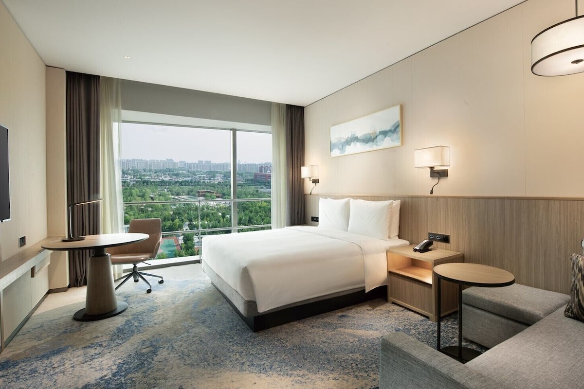 A hotel room with a large bed, a desk, a chair, a small table, and a TV.