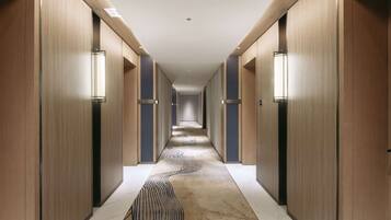 Un pasillo moderno de hotel con paneles de madera, puertas numeradas y alfombra estampada.