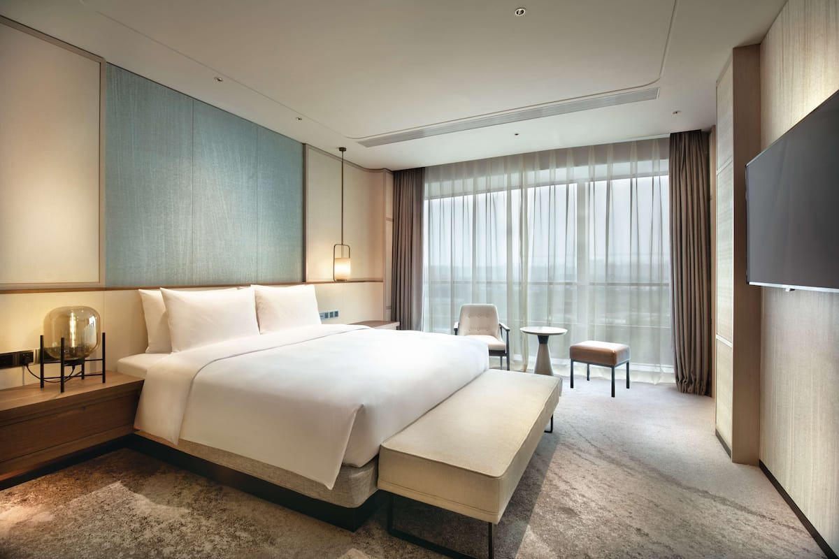 A modern hotel room with a large bed, bedside tables, a seating area, and a TV.