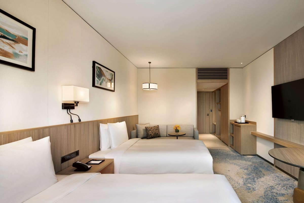 A hotel room with two beds, a TV, a desk, and a lamp.