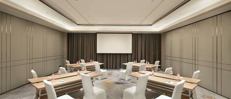A conference room with a large screen, multiple tables with chairs, and a carpeted floor.
