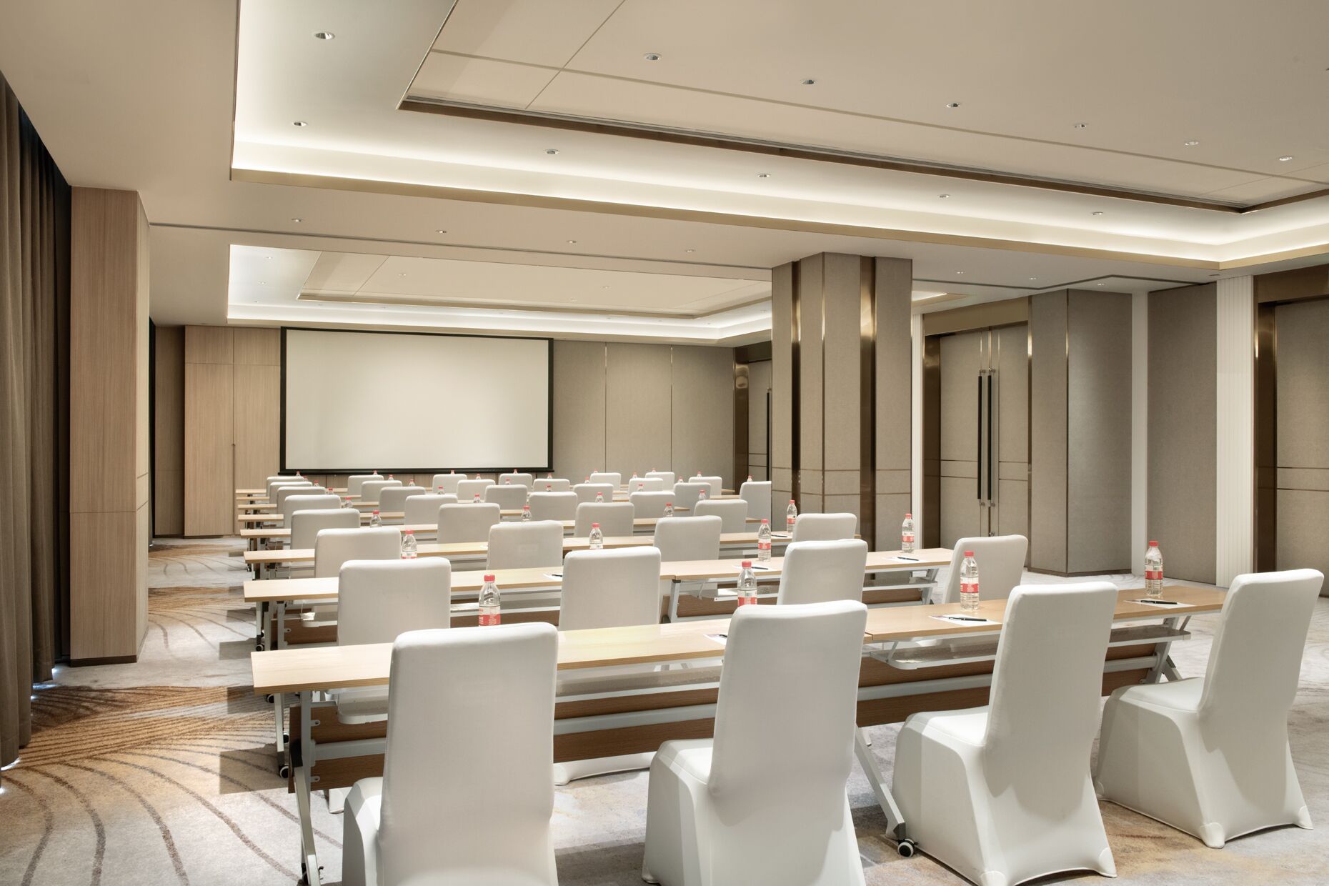 Un salón de conferencias con filas de sillas blancas, una pantalla grande y un atril.