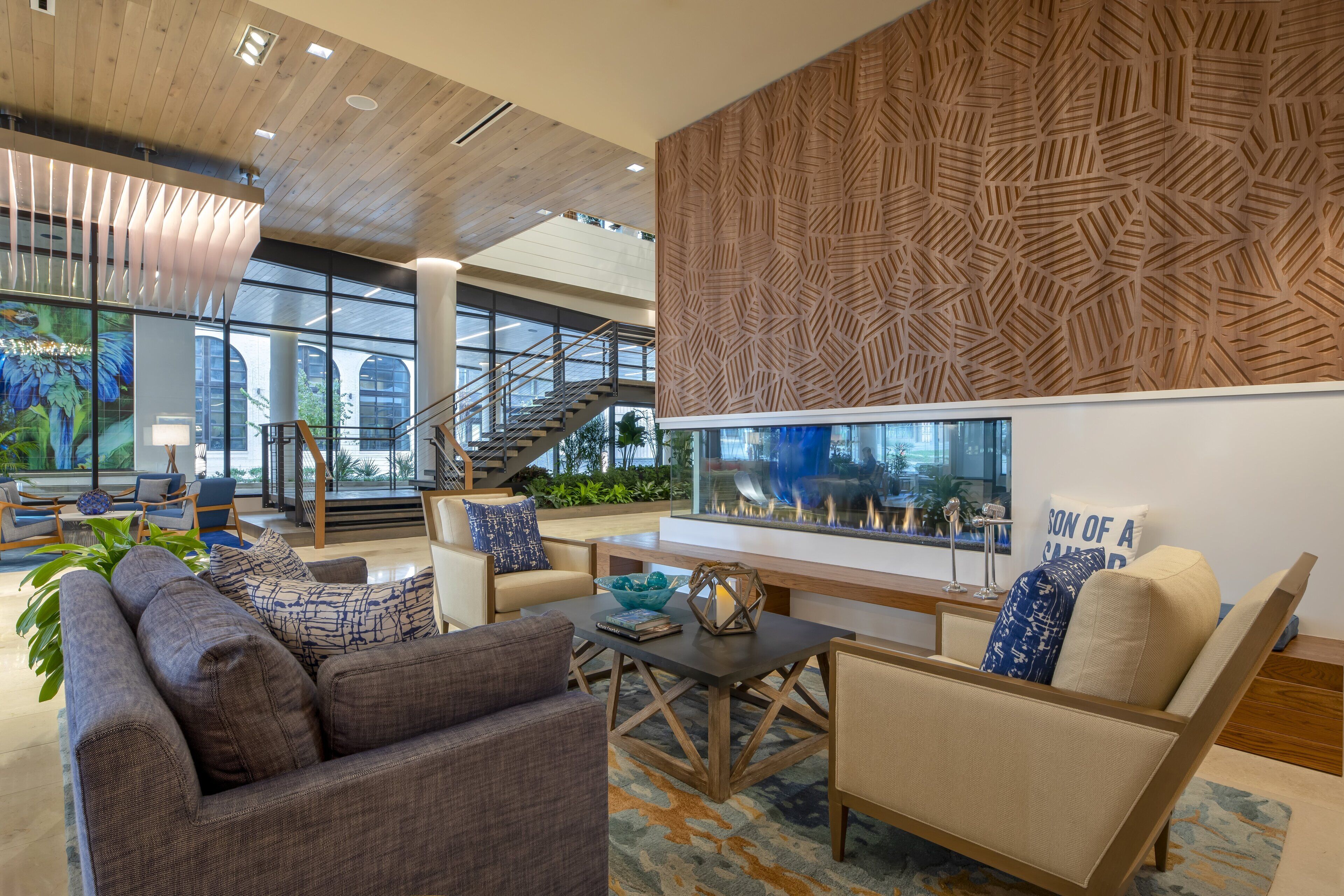 A modern lobby with a wooden ceiling, a large aquarium, comfortable seating, and a staircase.
