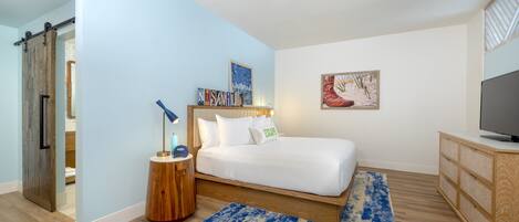 Une chambre à coucher avec un lit, une télévision, une armoire en bois, un tapis bleu et un tableau accroché au mur.