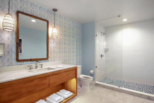Un baño moderno con tocador de madera, un espejo grande y una ducha con mampara de vidrio.