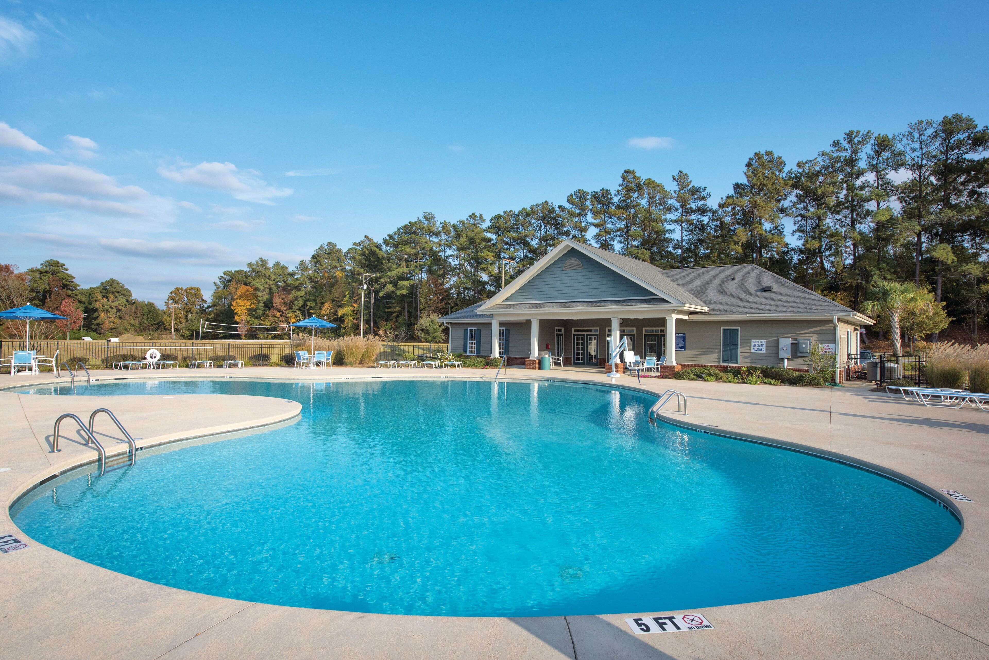 A large, clear swimming pool with a pool house in the background.