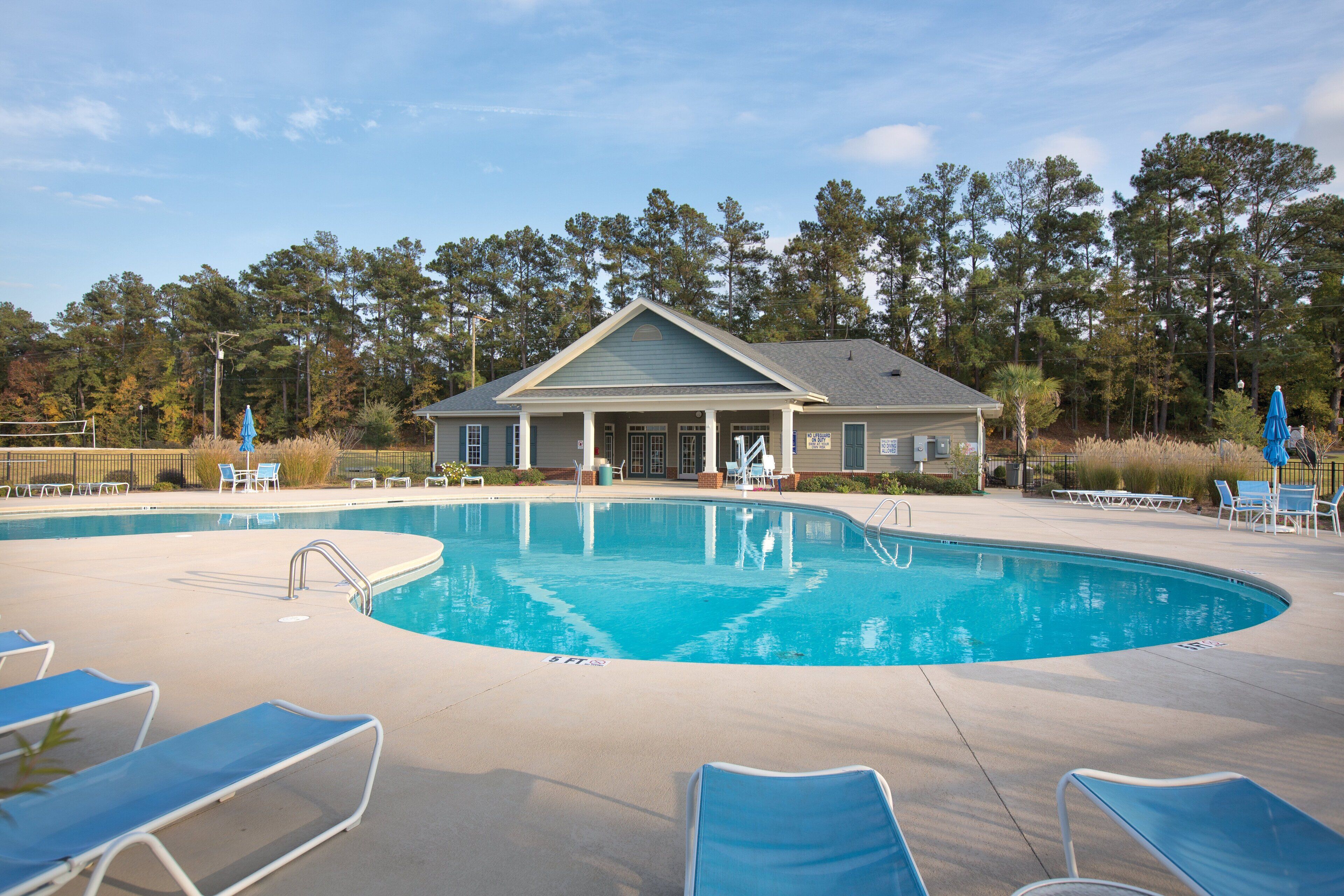 A swimming pool with lounge chairs, a building with a porch, and a forested background.