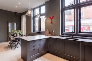 A modern kitchen with dark cabinetry, a large island with a sink, pendant lights, and a red lobster decoration on the wall.