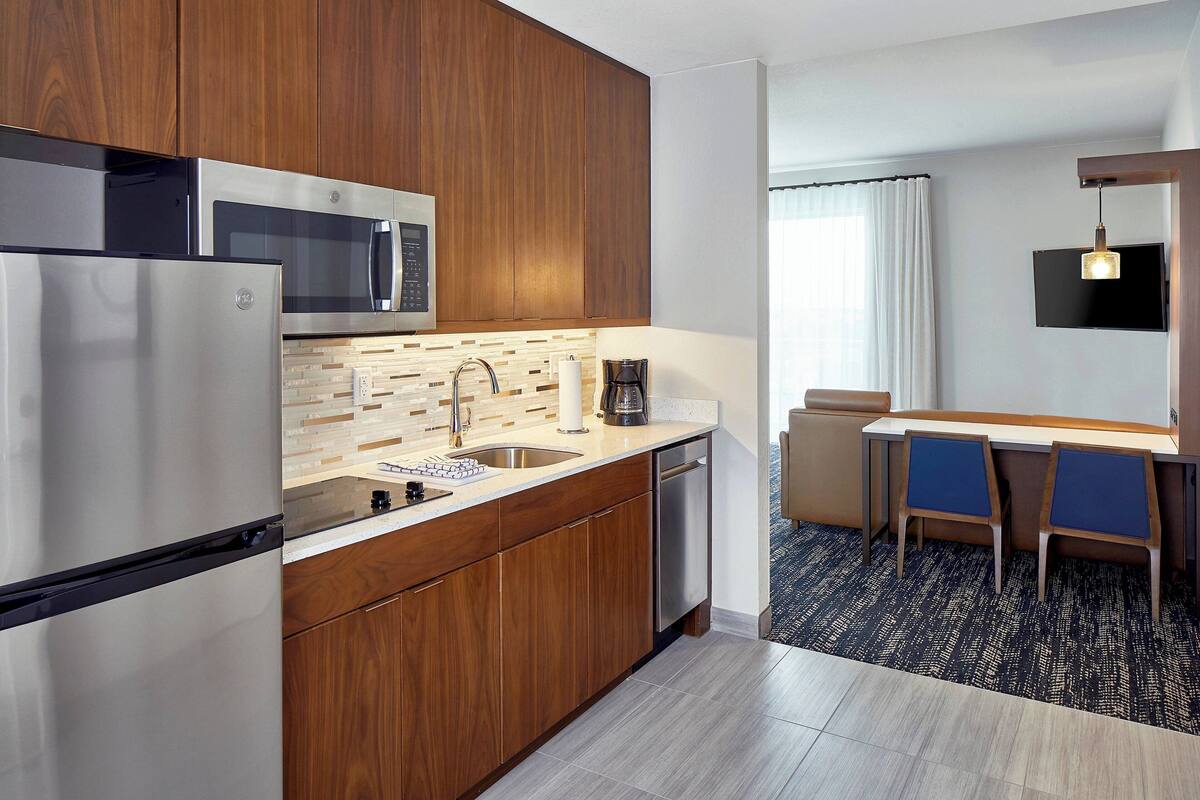 A modern kitchen with wooden cabinets, stainless steel appliances, and a dining area with two chairs and a table.