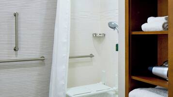 A bathroom with a shower, a bathtub, a handrail, and a shelf with towels.