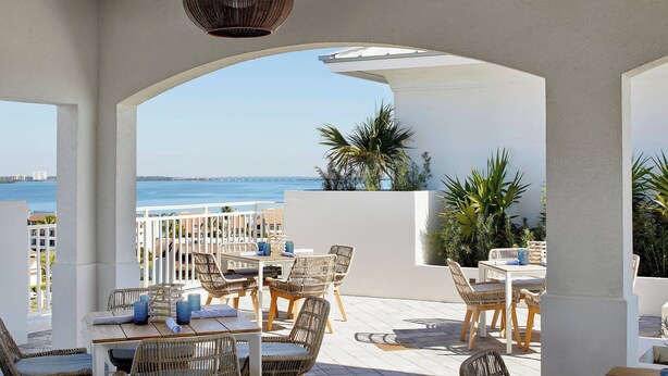An outdoor patio with wicker furniture, white columns, and a view of the sea. - Residence Inn by Marriott St. Petersburg Tierra Verde (Tierra Verde)