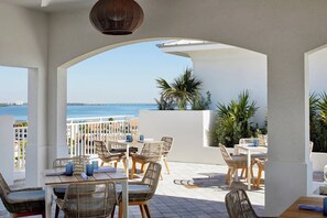 Un patio al aire libre con mobiliario de mimbre, columnas blancas y vista al mar.