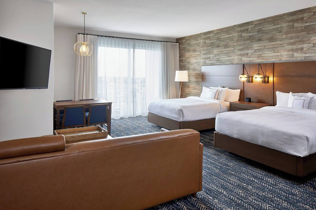 A hotel room with two beds, a sofa, a TV, and a desk.