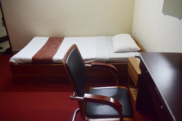 A small, simple room with a single bed, a wooden desk, and a chair. - Hotel Givenci International (Dhaka)