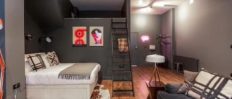 A modern bedroom with a loft bed, a sofa, a ladder, and a neon light.