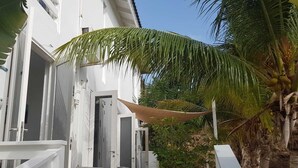 Un edificio blanco con una galería techada, palmeras y unidades de aire acondicionado al aire libre.