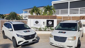 Dos SUVs blancos estacionados frente a un edificio con letreros de BBcuracao y CaribResidence.