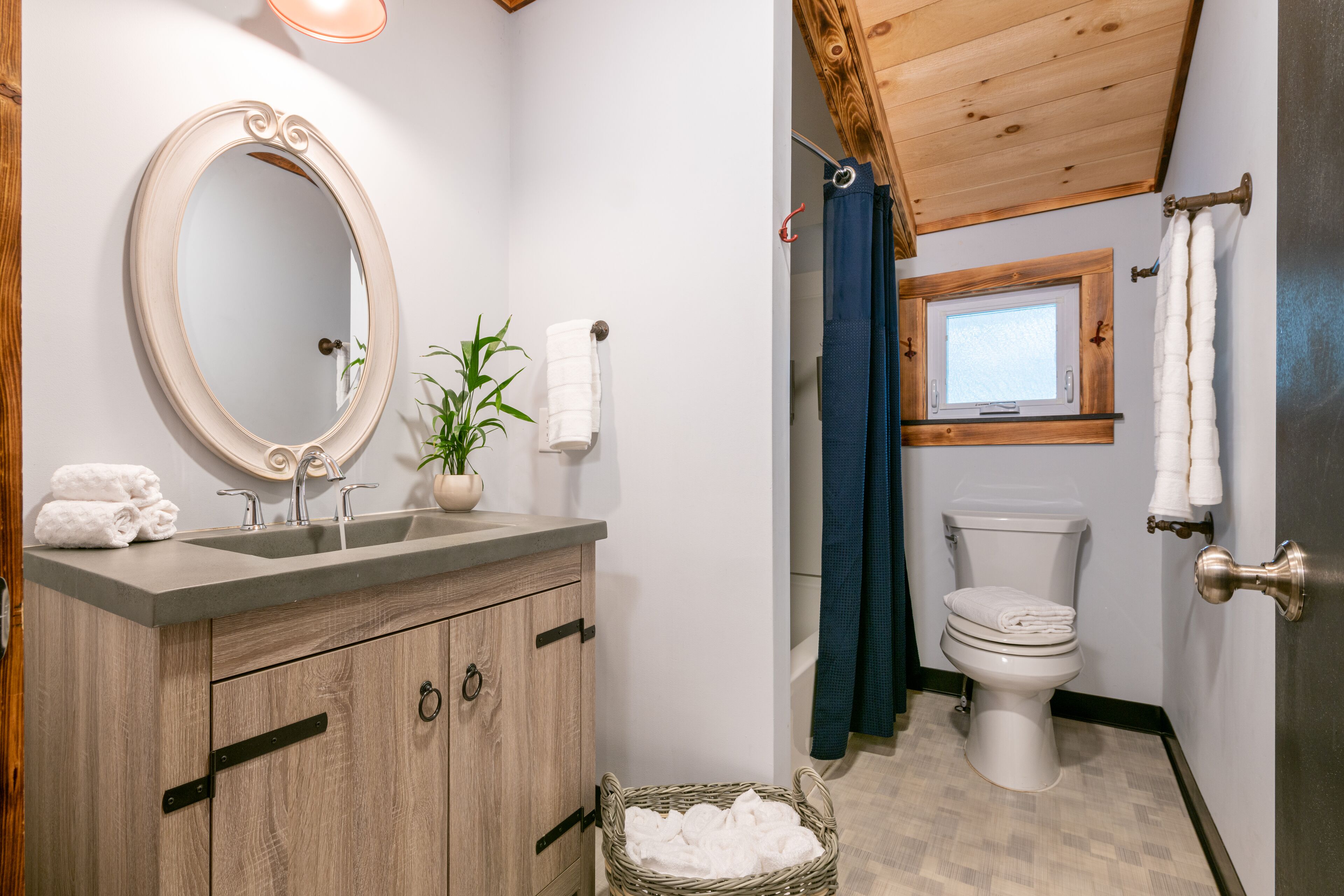 A bathroom with a wooden vanity, a round mirror, a sink, a toilet, and a window.