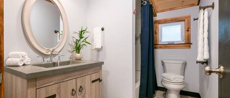 A bathroom with a wooden vanity, a round mirror, a sink, a toilet, and a window.