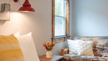 A cozy room with a wooden bench, a white cushioned chair, a small table with a vase of tulips, and a red wall lamp.