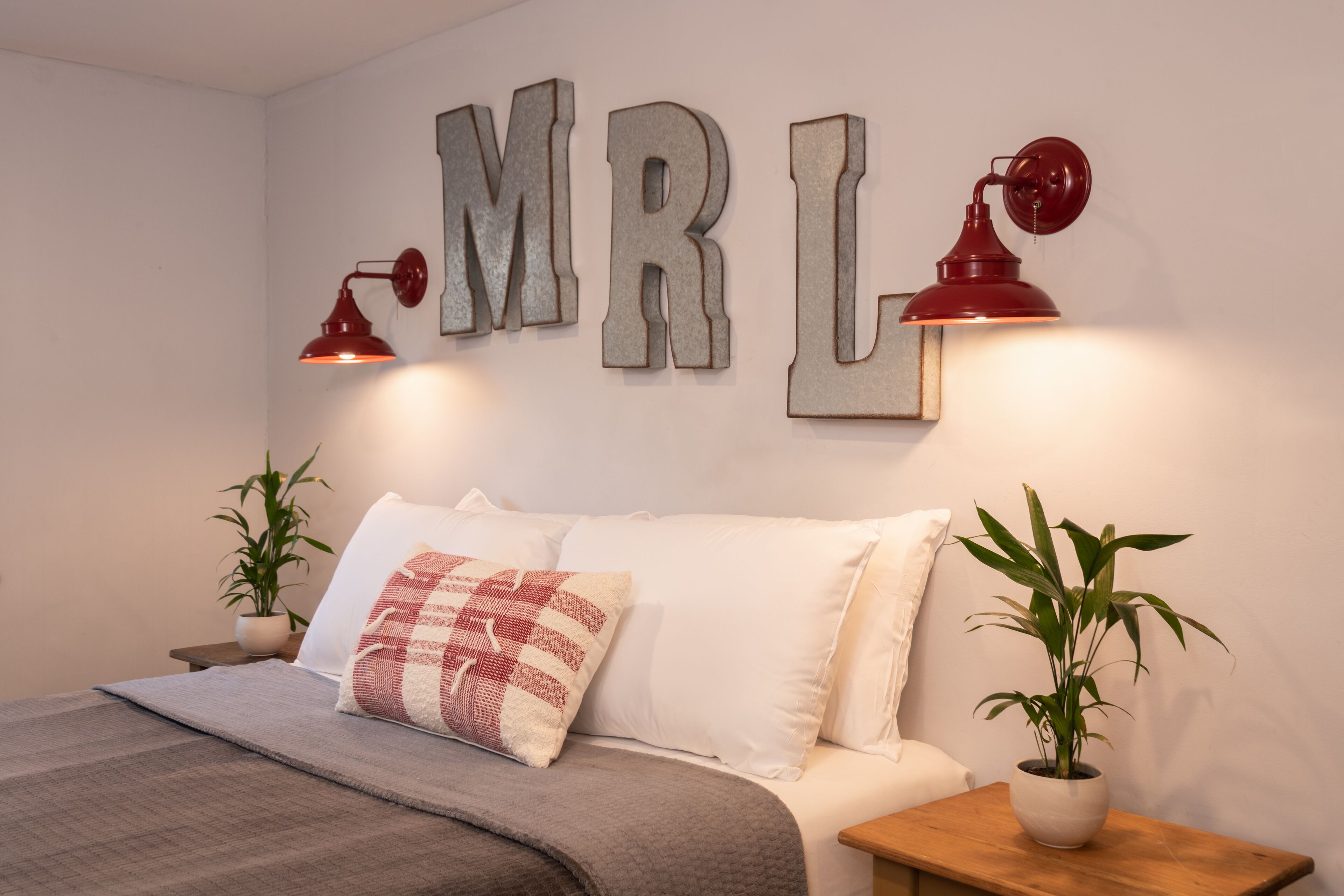 Un dormitorio con cama, almohadas, mesita de noche con lámpara y un cartel en la pared.