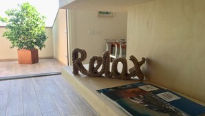 A room with a wooden floor, a potted plant, a 'Relax' sign, and a magazine on a table. - New Loft with beautiful lake view (Barcuzzi)