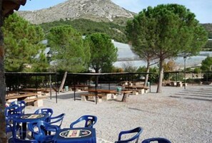 Una terraza con mesas al aire libre, una montaña al fondo y árboles.