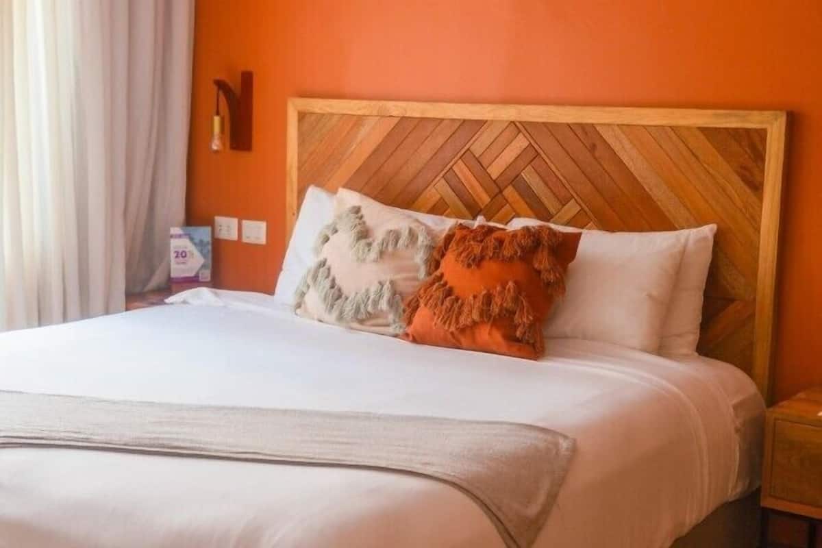 Una cama con cabecera de madera, ropa de cama blanca y dos almohadas decorativas.
