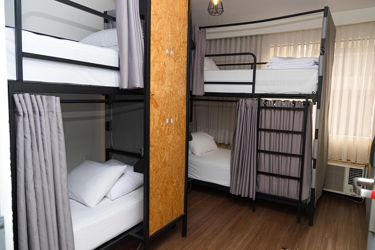 A dormitory room with bunk beds, wooden paneling, and a ceiling light fixture.