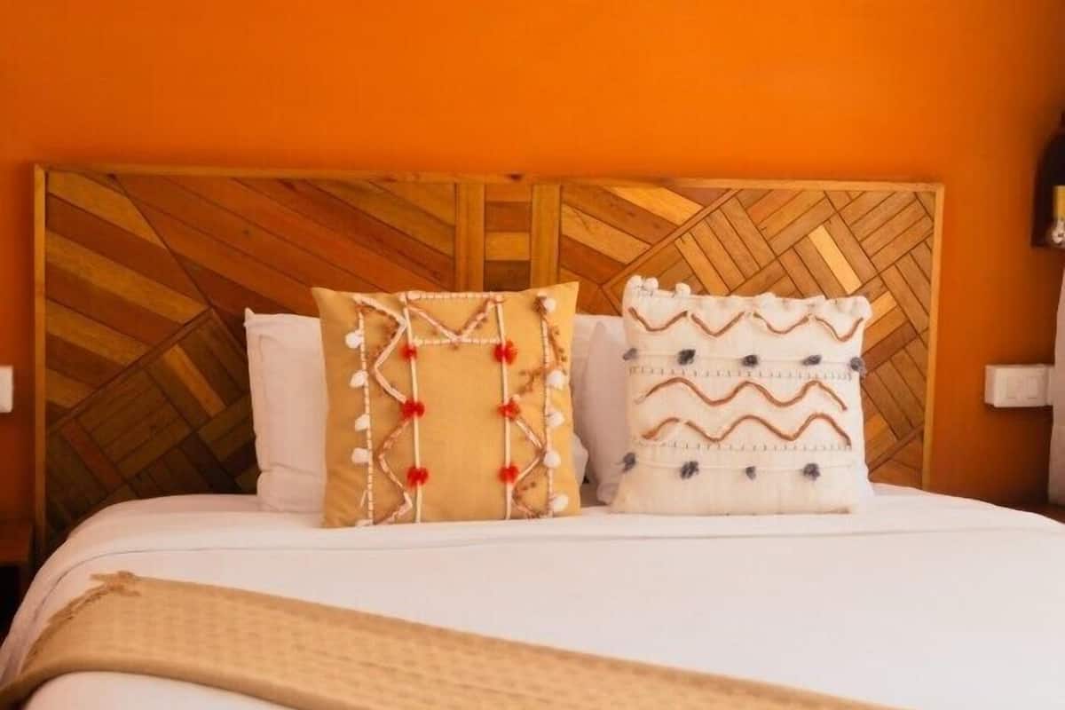 Una cama con cabecera de madera, dos almohadones decorativos y una colcha color beige.
