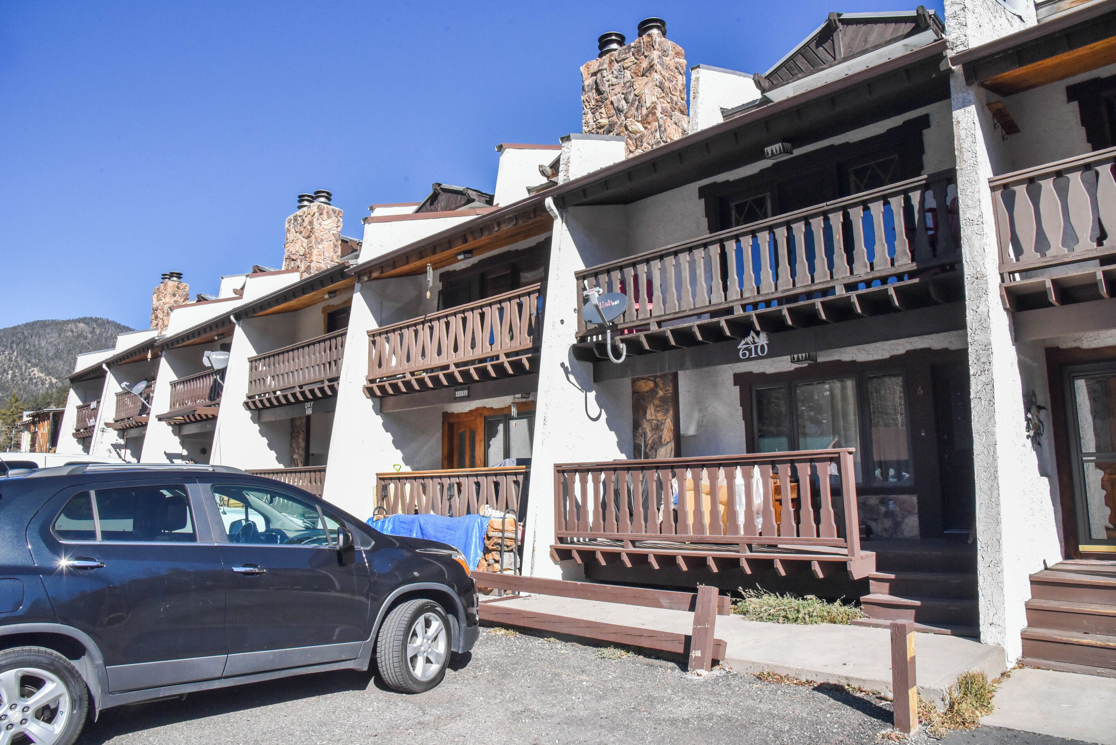 A row of traditional-style buildings with balconies, a parked car, and a clear blue sky.