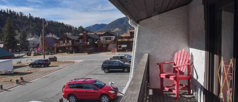Un balcón con una silla Adirondack roja, vistas a un estacionamiento con varios autos y un paisaje montañoso.