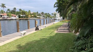 A waterfront walkway with a wooden dock, benches, and a grassy area.
