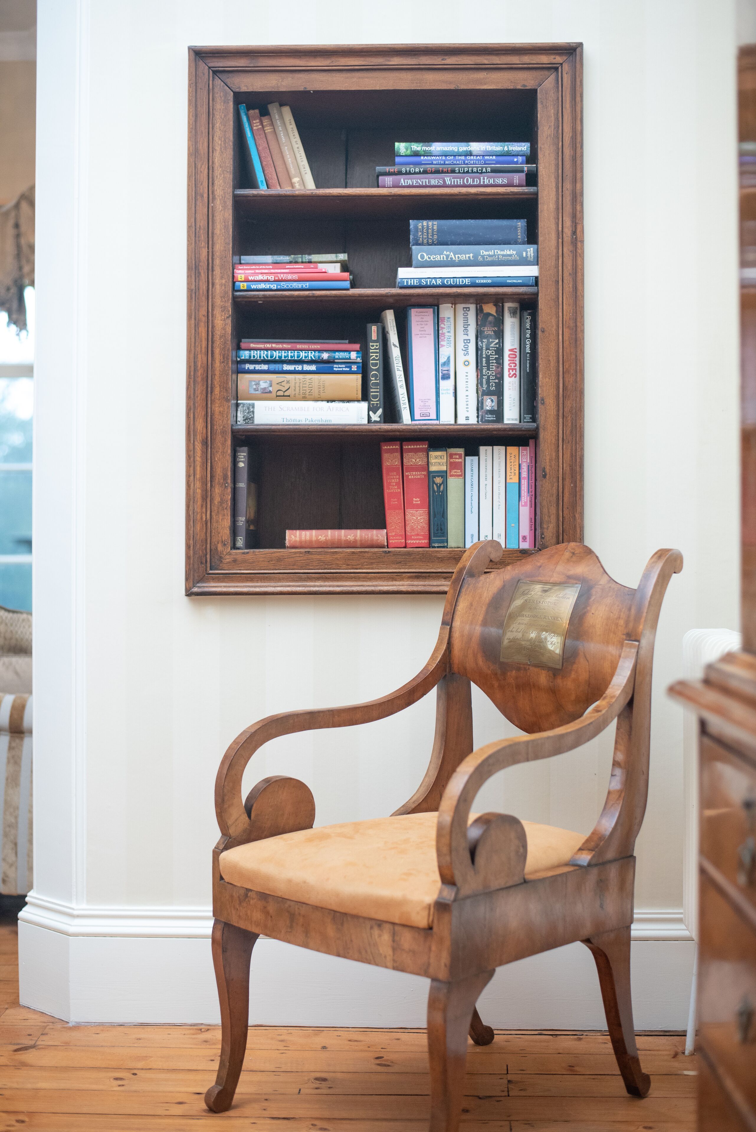 A wooden chair with a cushioned seat and backrest, positioned in front of a bookshelf filled with various books.