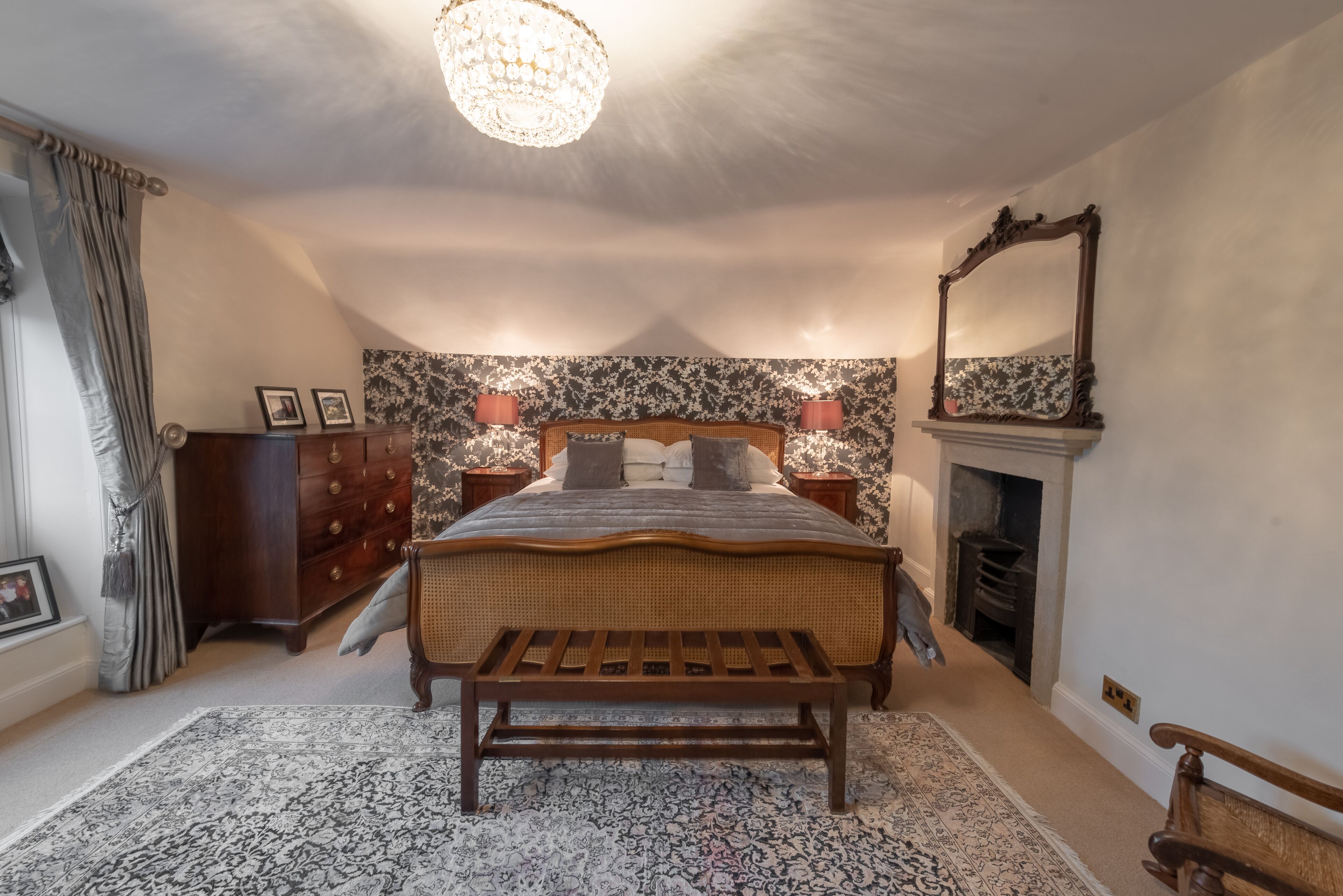 A bedroom with a large bed, a wooden bench, a fireplace, and a chandelier.