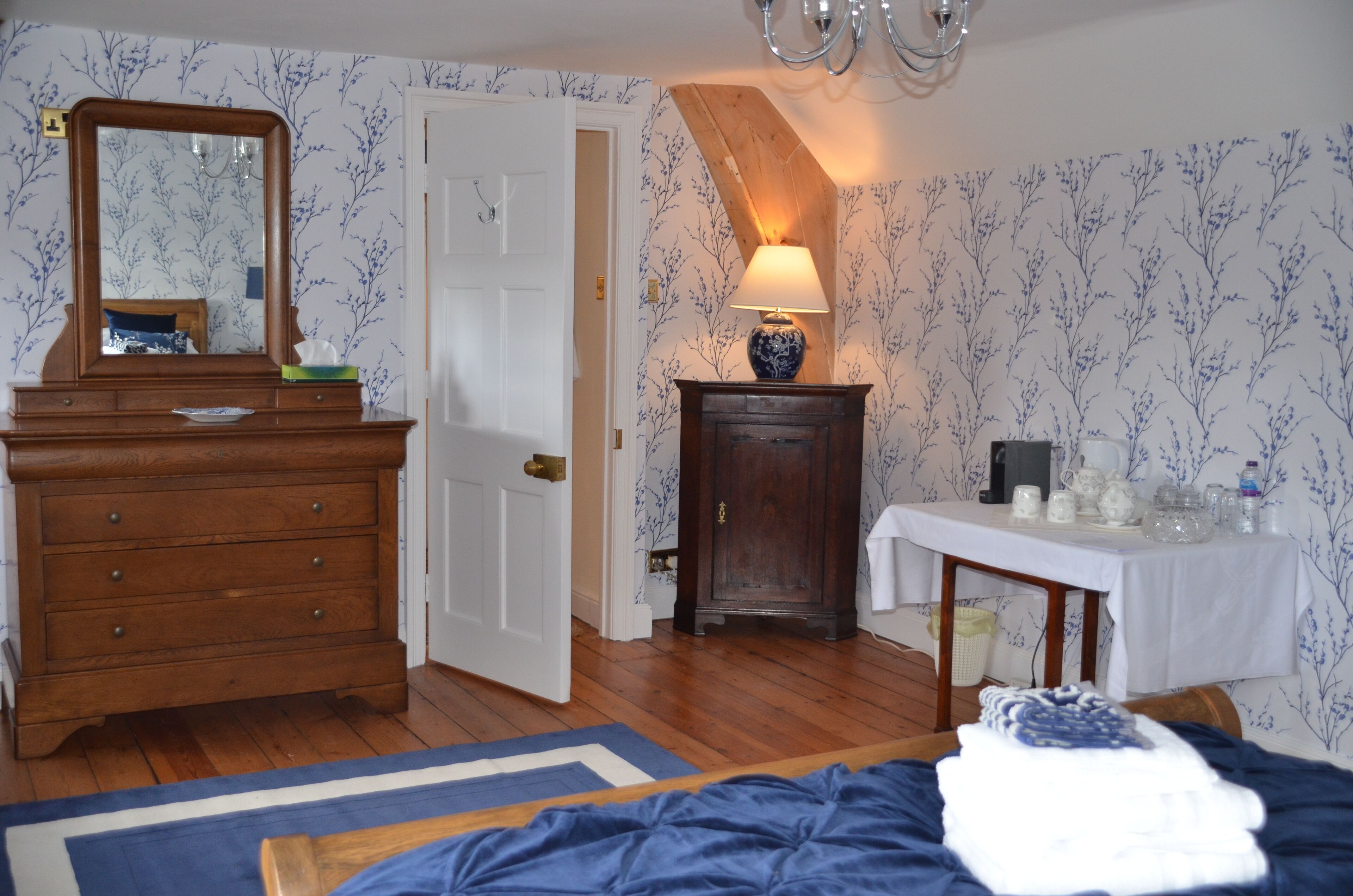 A bedroom with a wooden dresser, a bedside table with a lamp, and a bed with a blue blanket.
