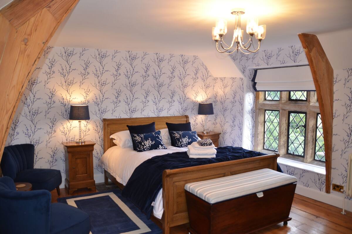 A bedroom with a wooden bed, two bedside tables, a bench, a chandelier, and a window with a view.
