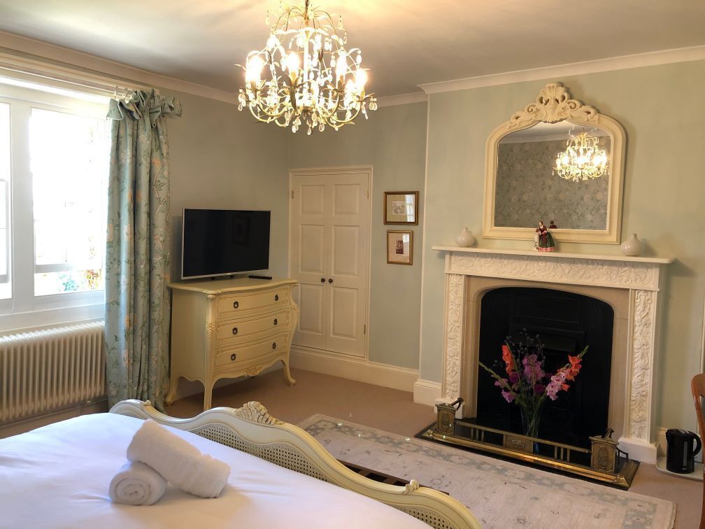 A bedroom with a bed, a television, a dresser, a fireplace, and a chandelier.