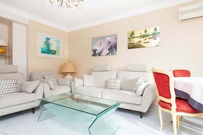 A living room with a glass coffee table, two sofas, a red chair, and wall art.