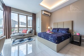A modern hotel room with a large bed, a sofa, a small table, and a view of the city.