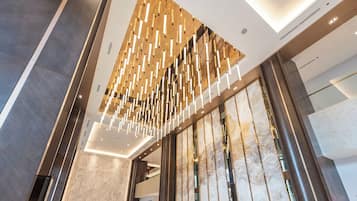 Un hall d’hôtel moderne avec un plafond haut, un comptoir d’accueil et une grande cloison en verre.