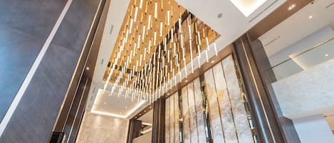 A modern hotel lobby with a high ceiling, a reception desk, and a large glass partition.