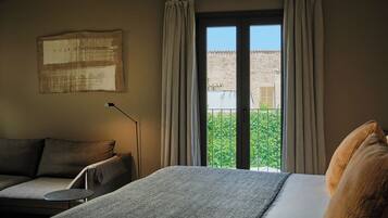 A room with a bed, a sofa, a standing lamp, and a balcony with curtains.