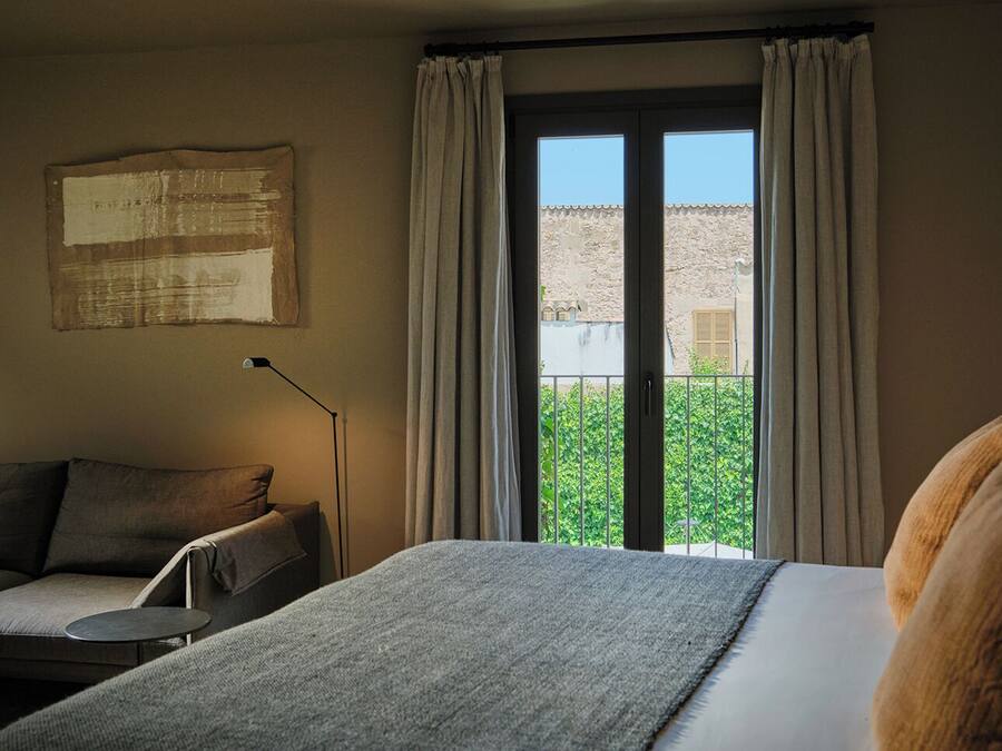 A room with a bed, a sofa, a standing lamp, and a balcony with curtains.
