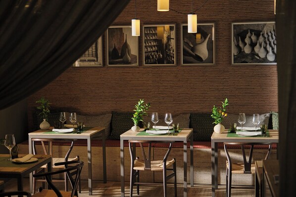 A restaurant with wooden panel walls, pendant lighting, and framed artwork. Tables are set with wine glasses and plates. - Can Aulí Luxury Retreat (Pollenca)